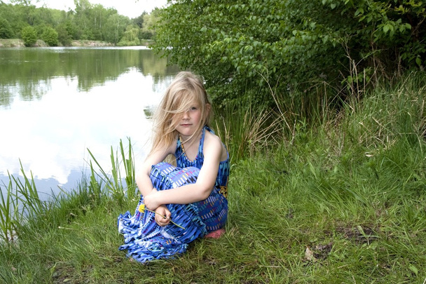 Girl sitting near the pond. Little blonde fairy. - Foto, imagen