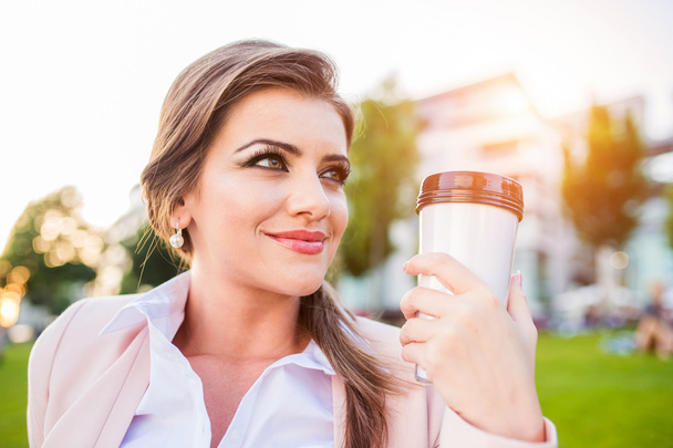 Businesswoman drinking coffee in park - Fotoğraf, Görsel