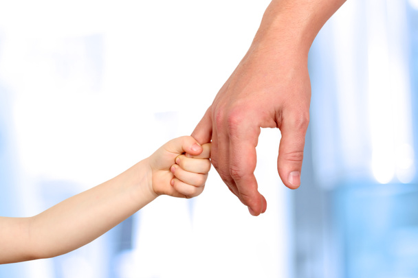 ein Vater hält die Hand eines kleinen Kindes auf blauem Hintergrund - Foto, Bild