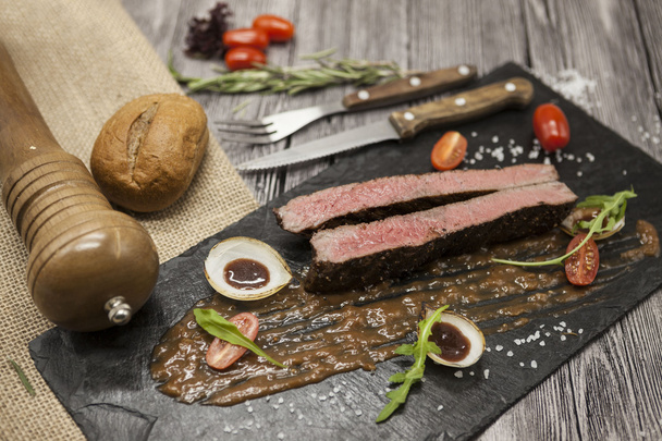 Ribeye steak márvány marhahús zöldségek és barbecue mártással. Szolgált egy tányér fekete kő villával és késsel . - Fotó, kép