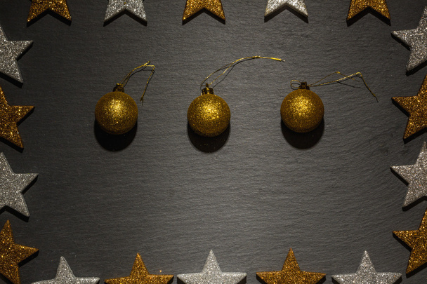 Τρία χρυσά στολίδια Χριστουγέννων σε μαύρο φόντο πλακών - Φωτογραφία, εικόνα