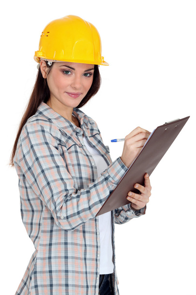 Female construction worker writing on her clipboard. - Zdjęcie, obraz