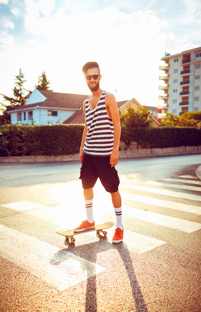 Стильний чоловік в сонцезахисних окулярах зі скейтбордом на вулиці в с
 - Фото, зображення