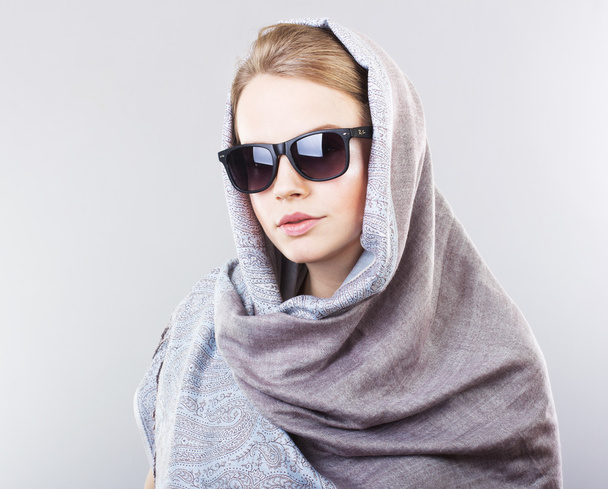 beautiful young woman in an embroidered shawl and sunglasses on a gray background - Foto, imagen