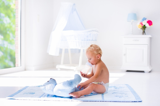 Poikavauva maitopullon kanssa aurinkoisessa lastenhuoneessa
 - Valokuva, kuva