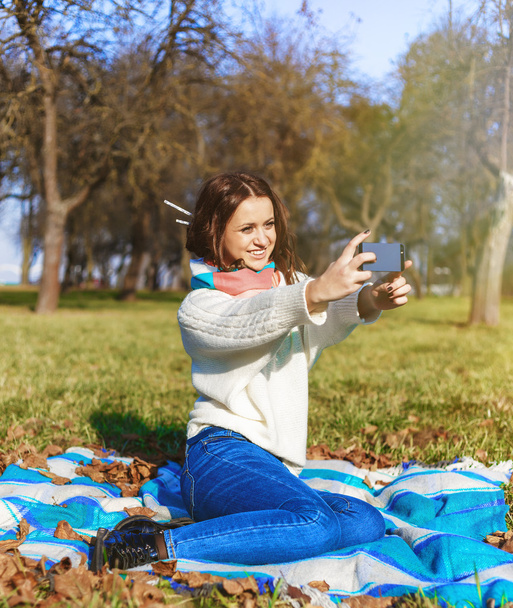 Stylish hipster smiling girl student with the mobile phone make selfie shot in the park outdoor - Foto, immagini