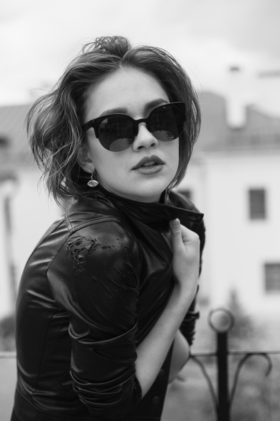 Chica con estilo en la chaqueta de cuero y gafas de sol al aire libre retrato en blanco y negro
 - Foto, imagen