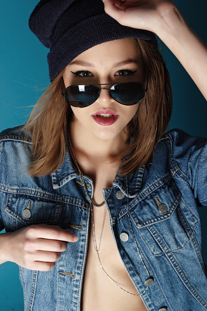 Stylish vogue rock girl in the jeans hat and sunglasses in the studio - 写真・画像