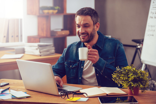 man working on laptop and holding coffee cup - Фото, зображення