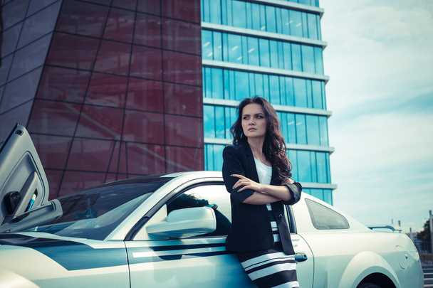 Kaunis liiketoiminnan nainen taustalla modernin toimiston lähellä urheiluauto
 - Valokuva, kuva
