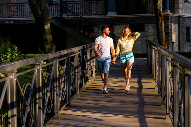 Εραστές τύπος και το κορίτσι με τα πόδια από μια γέφυρα στο πάρκο. - Φωτογραφία, εικόνα