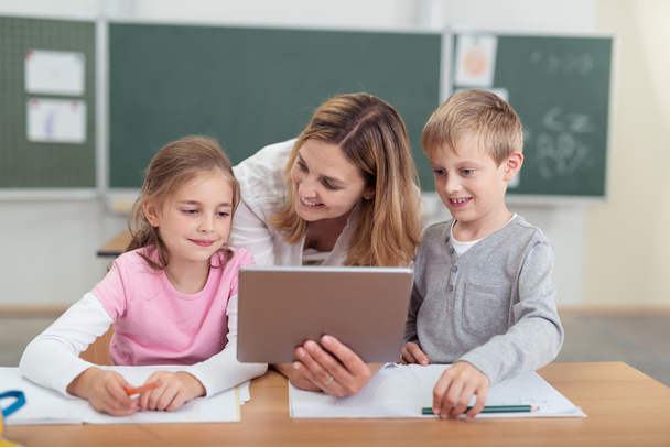 Teacher showing a tablet to two young students - Photo, image