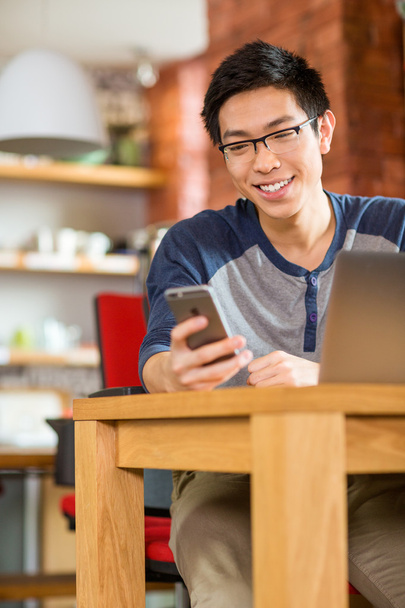 Щасливий усміхнений азіатський студент використовує ноутбук і мобільний телефон
  - Фото, зображення