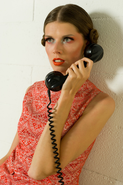 Girl calling on a old telephone dressed in orange on a sofa - Фото, изображение