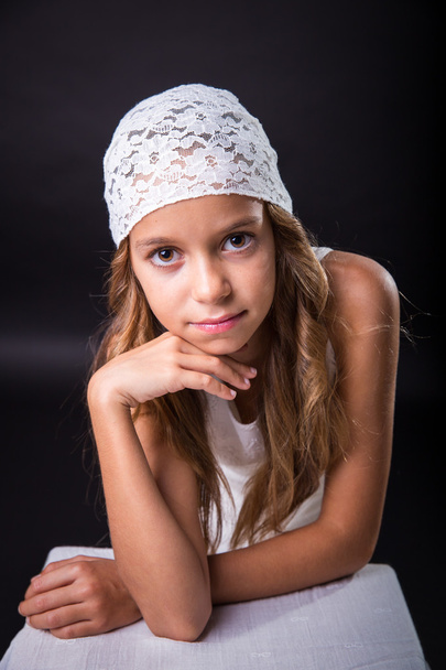 白い帽子と黒の背景の上に座って地味な外観を持つ少女 - 写真・画像