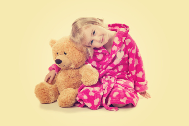 Маленька дівчинка в теплому рожевому халаті з ведмедем Тедді на білому ба
 - Фото, зображення