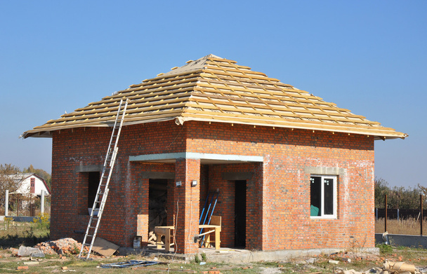 Στέγη μεμβράνη καλύμματα ξύλινη κατασκευή σπίτι πλαισιώνοντας με δοκών στεγών και μεταλλική σκάλα εξωτερική μπλε ουρανό. Κατασκευή εξωτερικού υλικού κατασκευής σκεπής με κόκκινο τούβλο σπίτι τοίχο προσόψεων. - Φωτογραφία, εικόνα