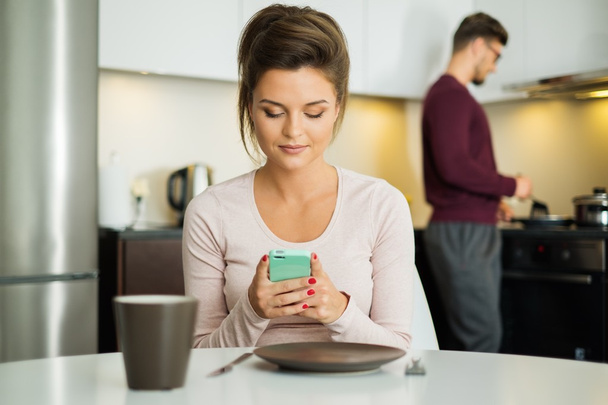 Žena s mobilním telefonem, čekání na jídlo v kuchyni doma  - Fotografie, Obrázek