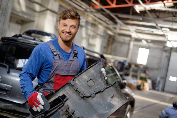 Mechanic with car bumper in a workshop - Zdjęcie, obraz