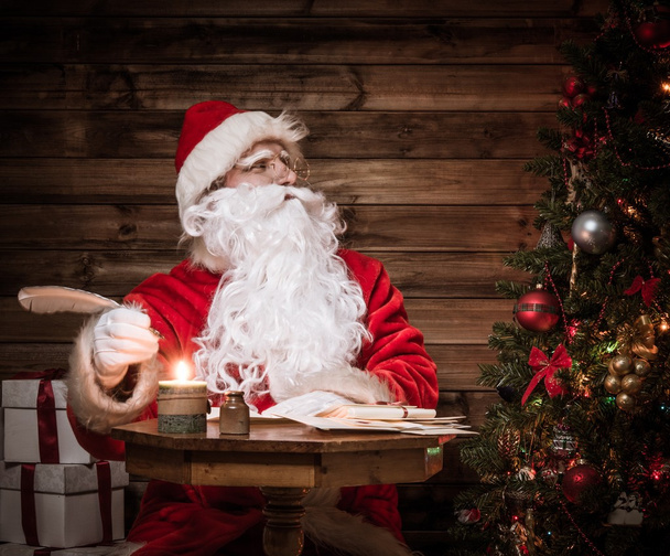 Weihnachtsmann im hölzernen Heim-Interieur sitzt hinter Tisch - Foto, Bild