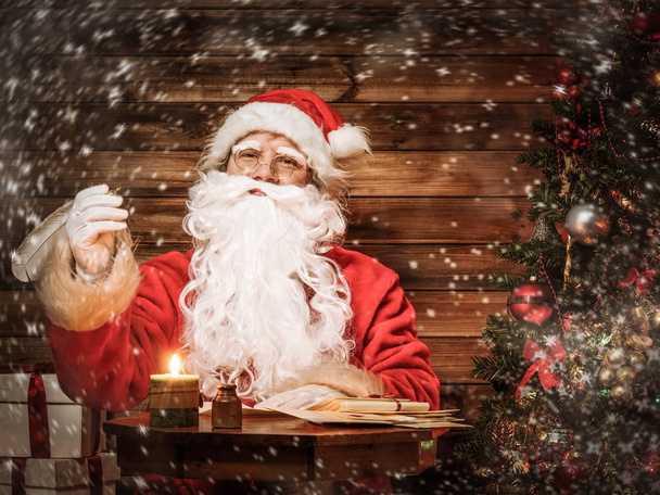 Санта-Клаус в деревянном интерьере дома сидит за столом
 - Фото, изображение