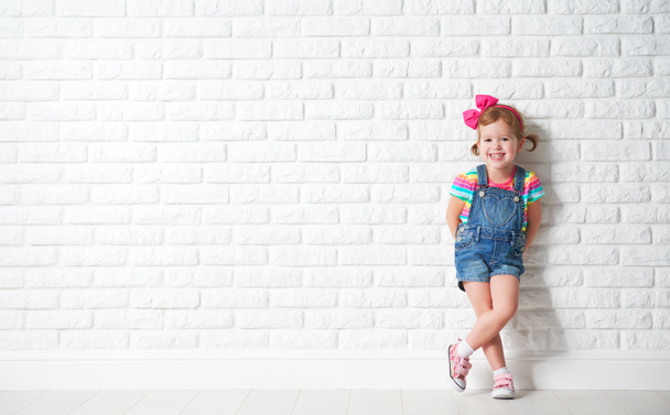 Niño feliz niña riéndose de la pared de ladrillo en blanco
 - Foto, imagen