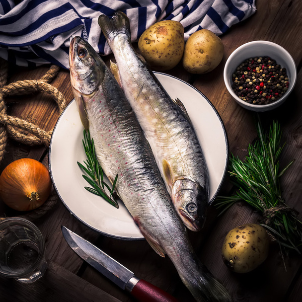 Ruwe riviervis met aardappelen, ajuin, specerijen en kruiden op een houten tafel.  - Foto, afbeelding