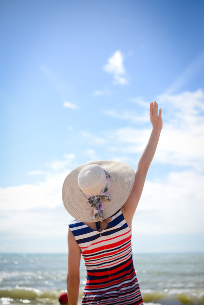 Mano ondeando elegante dama en sombrero de paja mirando al mar
 - Foto, imagen