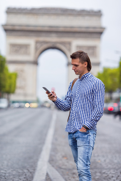 Nuori valkoihoinen mies pitelee puhelinta Champs Elyseessä Pariisissa.
 - Valokuva, kuva