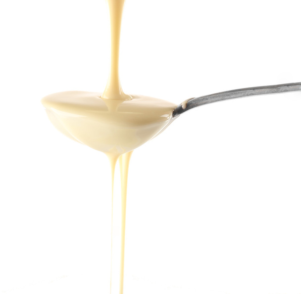 Condensed milk pouring from a spoon, isolated on white - Photo, image