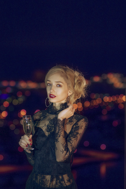 pretty lady with glass of champagne near window with night city on background - Foto, immagini