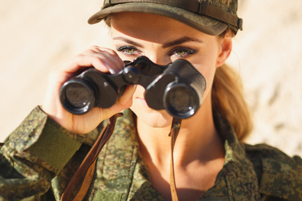 Gorgeous young woman in a Military costume with a binoculars on the background of a dessert - Foto, imagen
