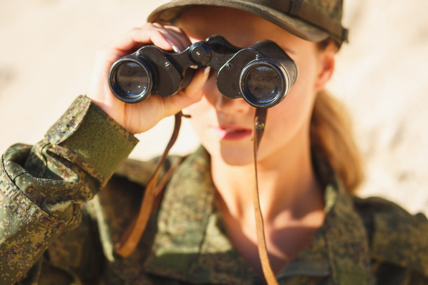 Hermosa joven con un traje militar con unos prismáticos en el fondo de un postre
 - Foto, imagen