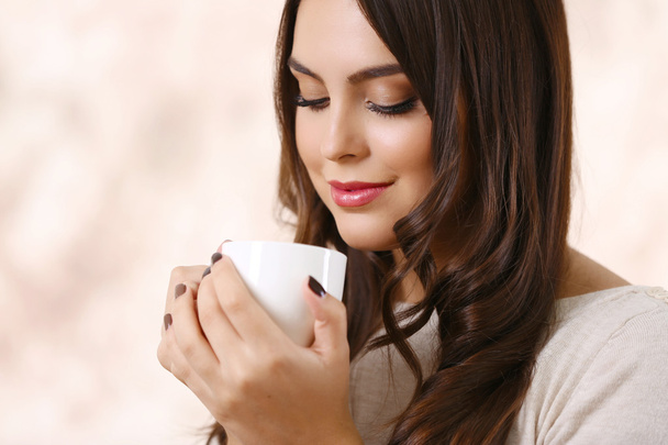 Portrait of young beautiful woman with cup of coffee on pink blurred background - Photo, image