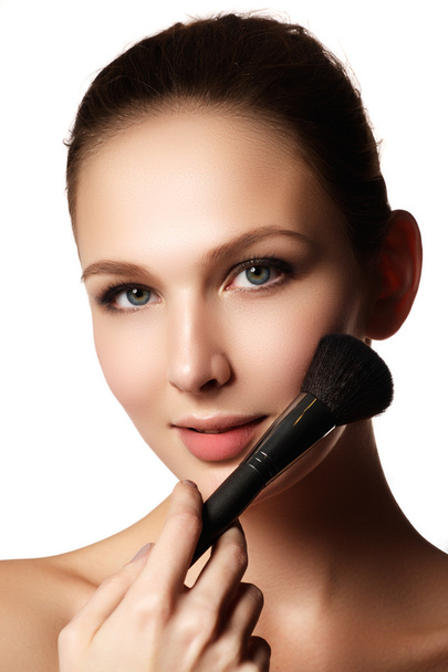 Beauty model with makeup brush. Bright make-up for brunette woman with blue eyes. Beautiful face. Perfect Skin. Applying makeup - 写真・画像