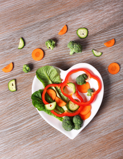 Useful cut vegetables on a plate in the form of heart on wooden table top view - Фото, изображение