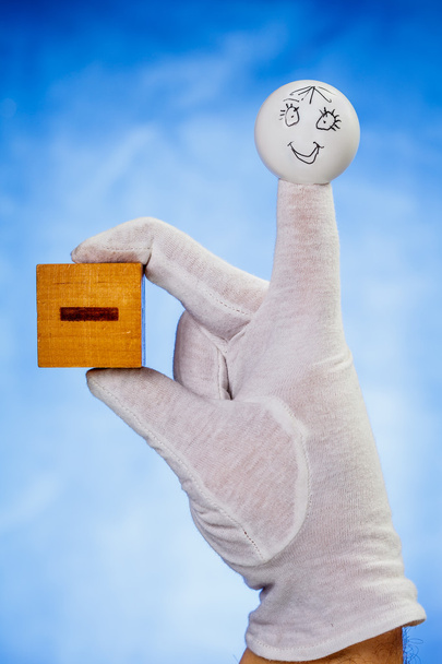 マイナス記号の付いた木製の立方体を保持している人形の指 - 写真・画像