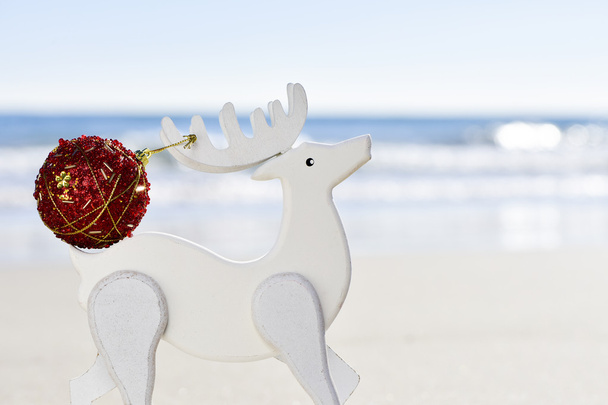 christmas ball in the antler of a wooden reindeer on the beach - Photo, Image