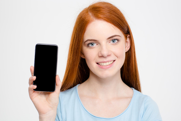 Charming cheerful young redhead woman showing blank screen of smartphone - Valokuva, kuva