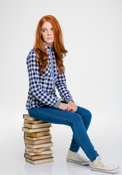 Thoughtful woman with red hair sitting on books and thinking - Фото, изображение