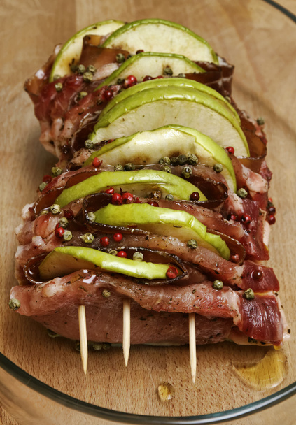 Итальянская еда, сырая говядина из свинины (ариста) с нарезанными яблоками, беконом и зеленым пе
 - Фото, изображение
