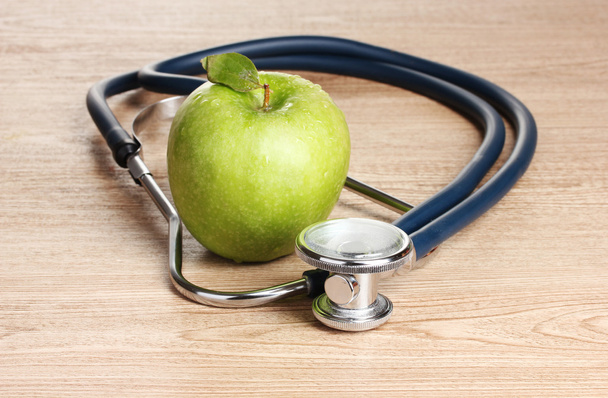 Medical stethoscope and green apple on wooden background - Фото, зображення