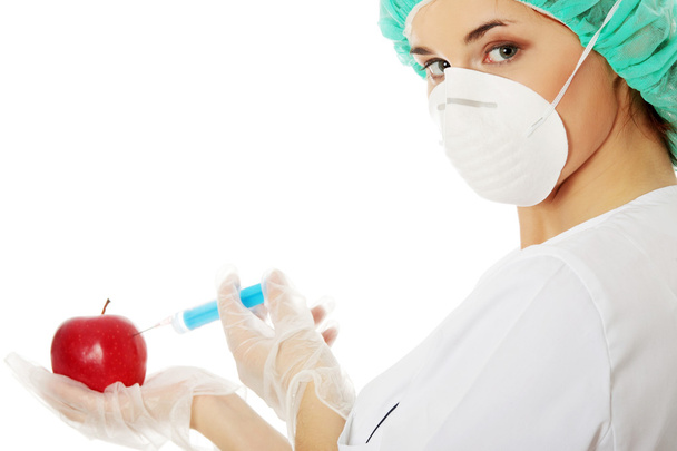 Woman in white coat with syringe and apple (biotechnologist) - Foto, Bild