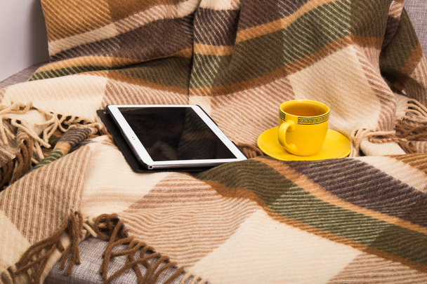  cup with tea and the tablet on a checkered woolen plaid - 写真・画像