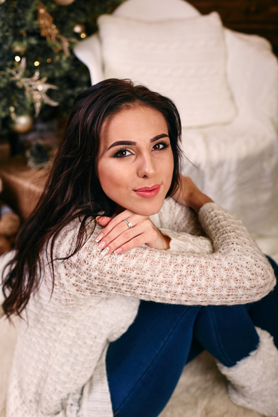 Портрет молодой женщины, сидящей возле рождественской елки
 - Фото, изображение