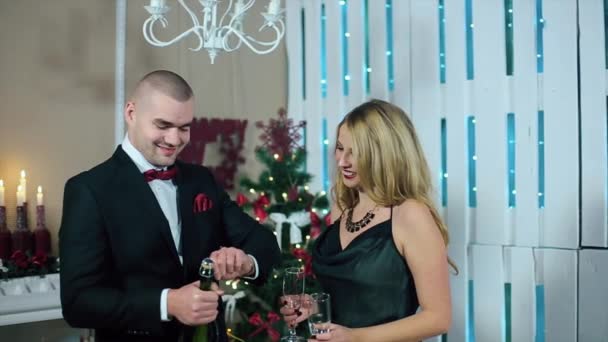 Happy Man in Suit and Woman in Evening Dress Champagne explosion in a white room with fireplace and Christmas tree - Felvétel, videó