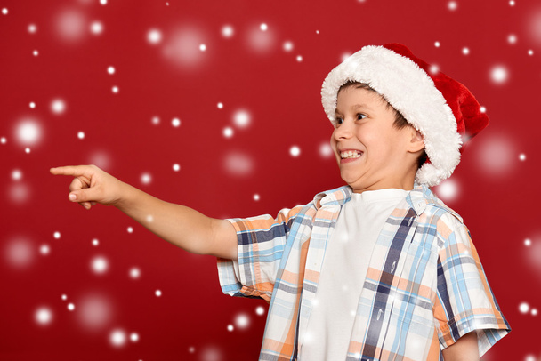 Weihnachtskonzept für den Winterurlaub - Junge mit Weihnachtsmannmütze zeigt auf sein Handy - Foto, Bild