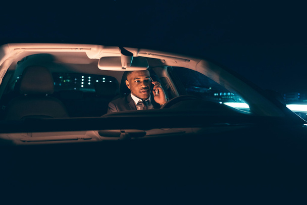 Mies pukeutunut pukuun autossa yöllä
 - Valokuva, kuva