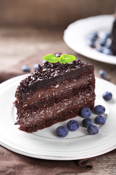 Schokoladenkuchen mit Schokoladencreme und frischen Blaubeeren auf Teller, auf Holzgrund - Foto, Bild