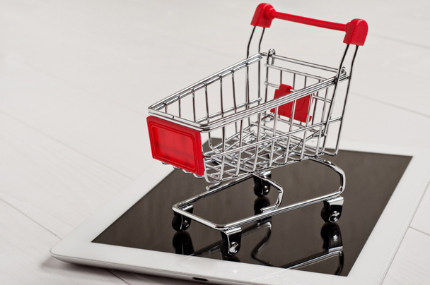 Primer plano pequeño carrito de compras en una tableta blanca
 - Foto, imagen
